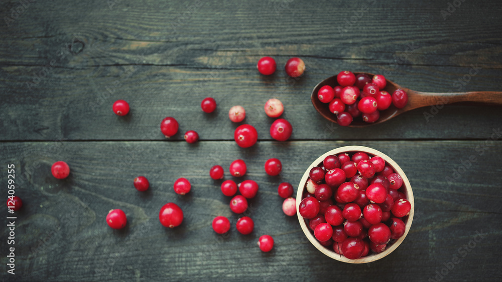 Fresh juicy cranberry in wooden round bowls with a wooden spoon on a table, top view Fresh juicy cranberry in wooden round bowls with a wooden spoon on a table, top view