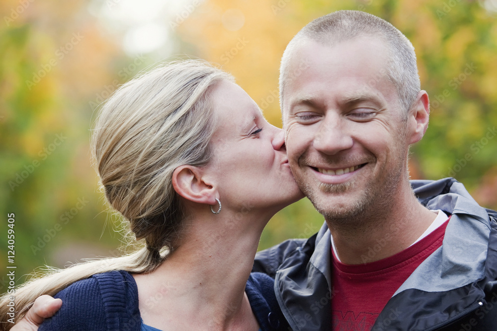 Wife Kissing Husband On The Cheek In A Park In Autumn; Edmonton, Alberta, Canada Wife Kissing Husband On The Cheek In A Park In Autumn; Edmonton, Alberta, Canada