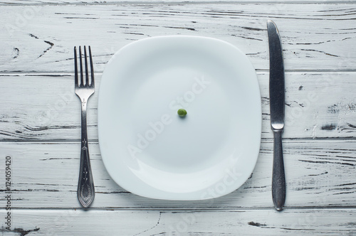 One small green pea on theempty plate.
Food for a girl on a diet. Very little food for lunch, breakfast or dinner.
