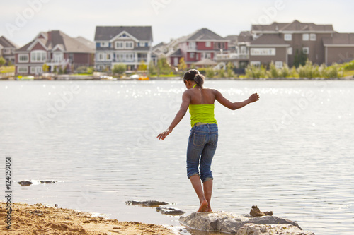 Teenage Girl Walking On The Rocks Along The Shore Of A Residential Lake; Edmonton, Alberta, Canada photo