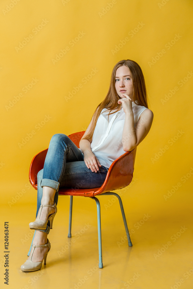 Young beautiful woman sitting on chair over yellow background. Young beautiful woman sitting on chair over yellow background.