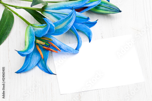 blue  lilies on the white table with sheet of paper