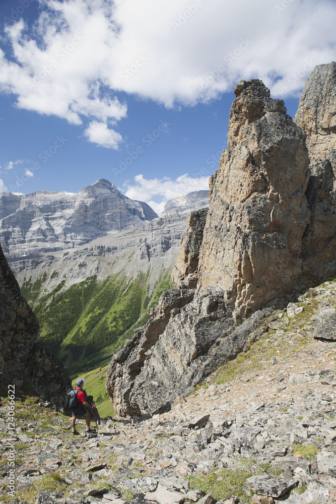 Male Hiker In The Distance On Rocky Trail With Large Sentinels And Mountains In The Background With Blue Sky And Clouds; Alberta, Canada Male Hiker In The Distance On Rocky Trail With Large Sentinels And Mountains In The Background With Blue Sky And Clouds; Alberta, Canada