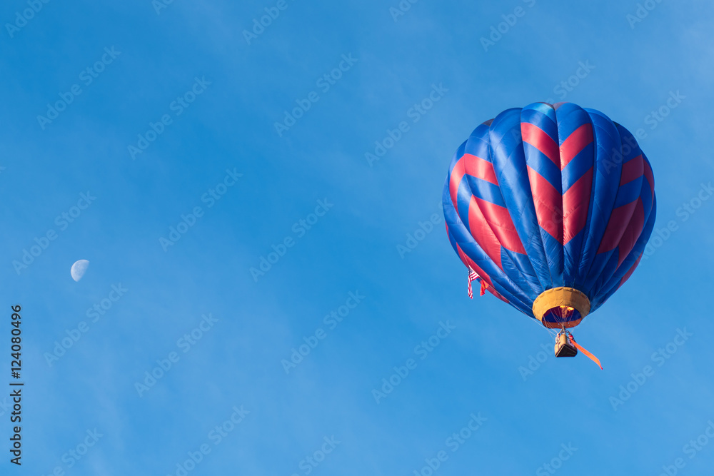 Naklejka premium This is a photo of a beautiful hot air balloon slowly sailing through a calm blue sky with the moon in the background.