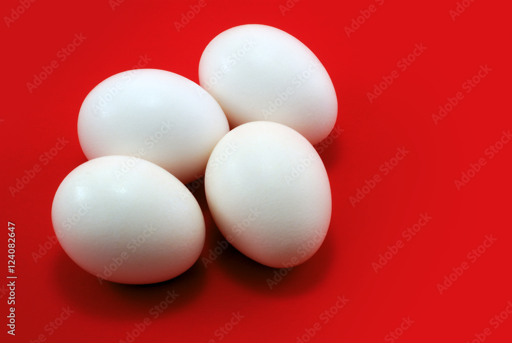 four white eggs on red background, horizontal studio shot four white eggs on red background, horizontal studio shot