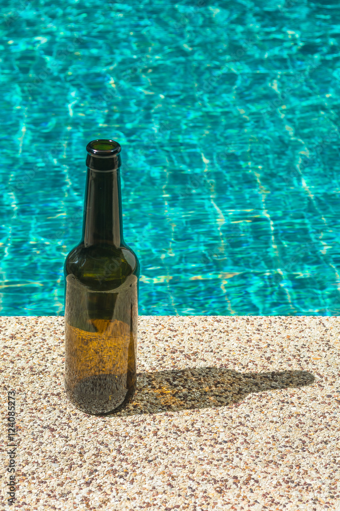 Long brown bottle next to the swimming pool in sunny day. Long brown bottle next to the swimming pool in sunny day.