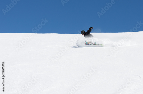 Snowboarder carving a turn on a blue sky day.