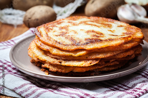 Stack of potato pancakes on a wooden table. In the background po