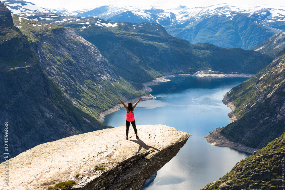 Young woman relaxon Trolltunga. Happy girl enjoy beautiful lake and good weather in Norway.