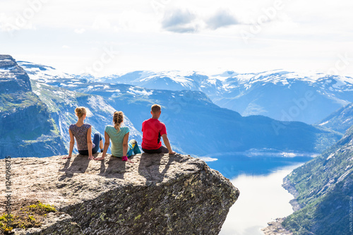 Happy friends relax on Trolltunga. People enjoy beautiful lake and good weather in Norway.