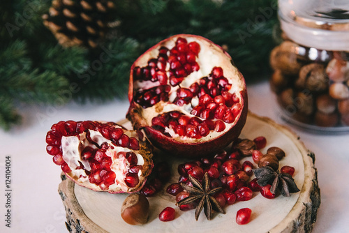 A close picture of a pomegranate in a winter composition, green tree branches and nuts in a jar on the background. Symbol of New Year and Christmas