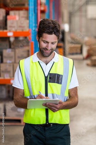Happy warehouse worker writing on clipboard