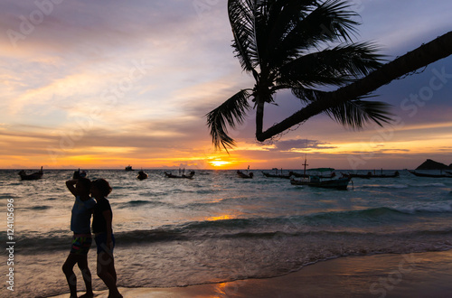 Beautiful sunset by the beach. Silhoette of coconut tree and tourists posing for photo at Tao Island  Thailand. Romantic vacation getaway.