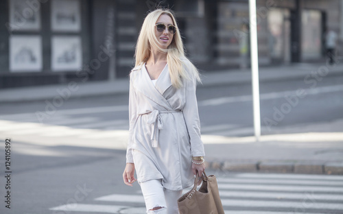 blonde woman in white jeans and coat walking on the city street