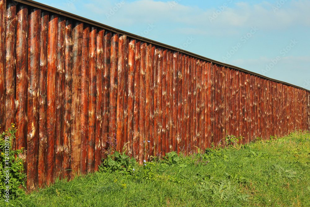 Long wooden fence made of oak tree trunks on green grass Long wooden fence made of oak tree trunks on green grass