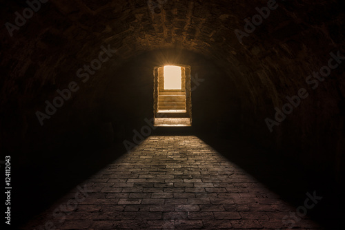 Basement interior with stone floor - Medieval European basement interior, with round ceiling and stone floor, with strong sun lights at the entrance photo
