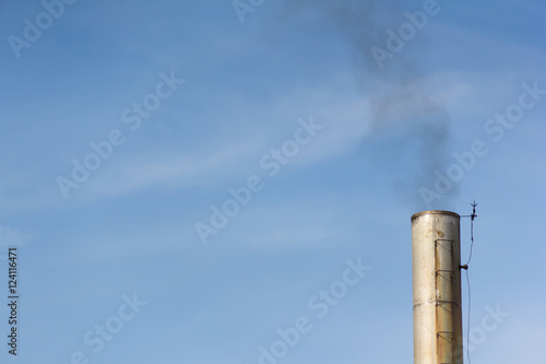 silver smoke stack with black smoke against blue sky 