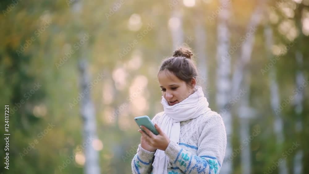 Smiling woman in a knitted sweater and scarf using mobile phone in park during the autumn. 1920x1080 Smiling woman in a knitted sweater and scarf using mobile phone in park during the autumn. 1920x1080