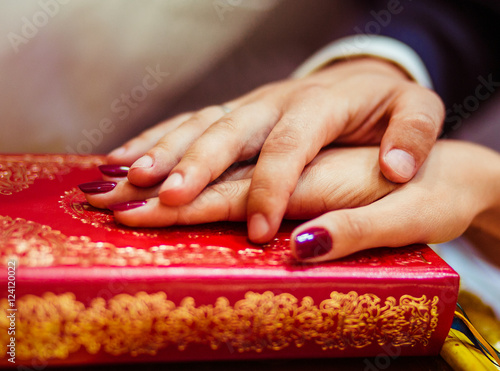 Groom holds his hand over bride's one on the red Bible