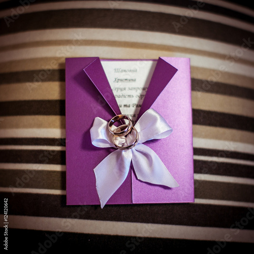 Wedding rings lie on the violet invitation letter