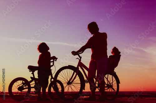 Biker family silhouette, father with two kids on bikes at sunset