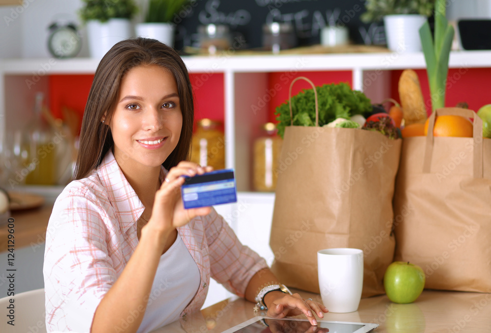 Smiling woman online shopping using tablet and credit card in kitchen Smiling woman online shopping using tablet and credit card in kitchen