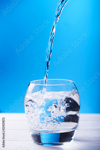 Pouring water with spashes in glass at a blue background