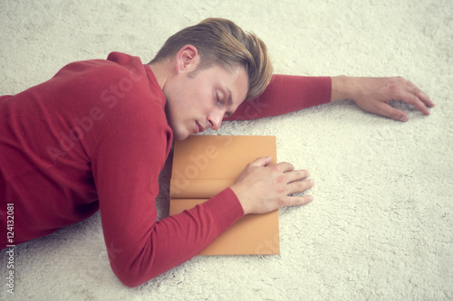 blond man sleeping on carpet and holding a book