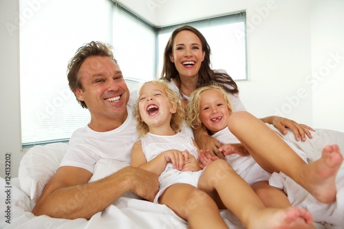 Cheerful young family with children relaxing on bed