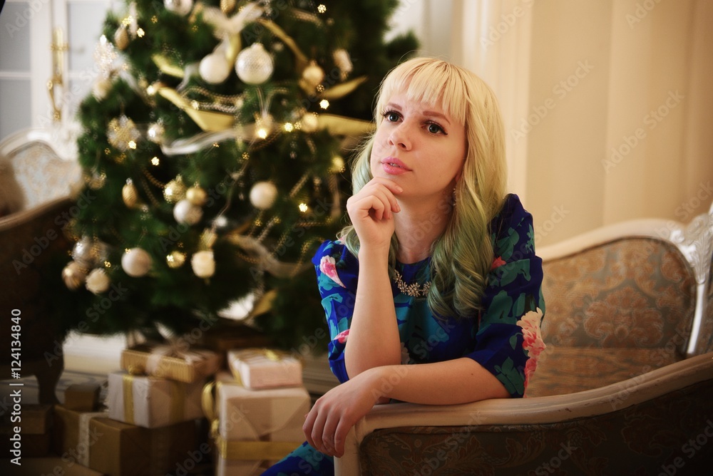 Beautiful young girl sits on sofa near Christmas tree with presents and dreams Beautiful young girl sits on sofa near Christmas tree with presents and dreams