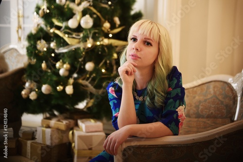Beautiful young girl sits on sofa near Christmas tree with presents and dreams