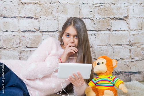 Beautiful girl with tablet. Modern learning, textbooks in electronic form on tablet. Girl listening to music on headphones. Electronic books, games on the tablet, shopping online. teen girl at home    © NatBud
