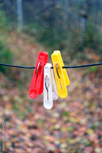Three colored clothepins hanging on black rope on a blurred background in autumn day outdoors closeup