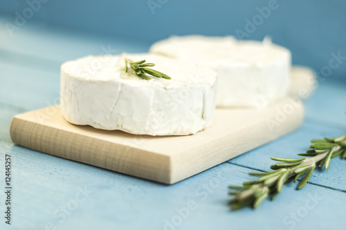 Round camembert cheese mold with rosemary on wooden board