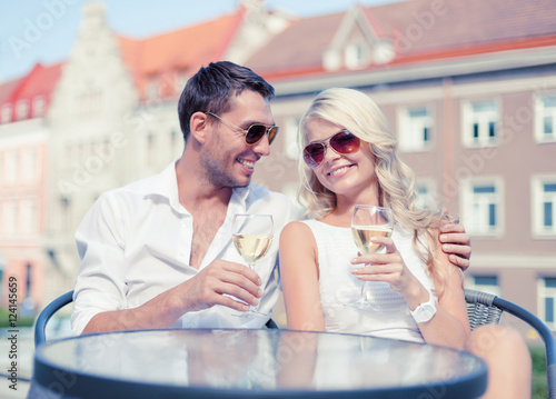 smiling couple in sunglasses drinking wine in cafe