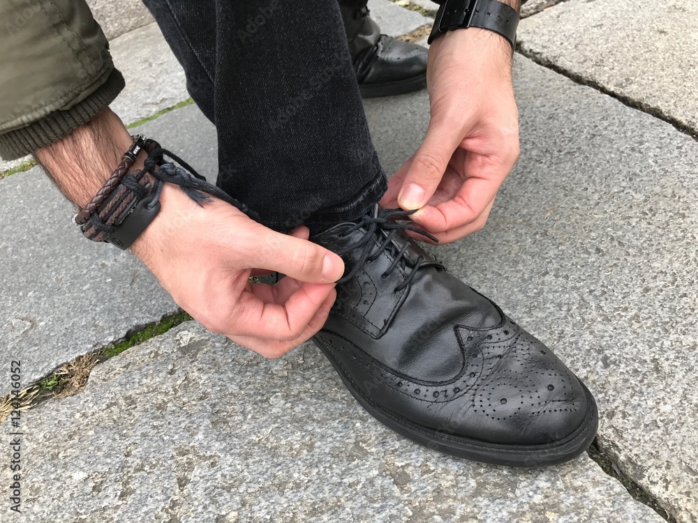 Man tying shoelaces in the street, black shoes