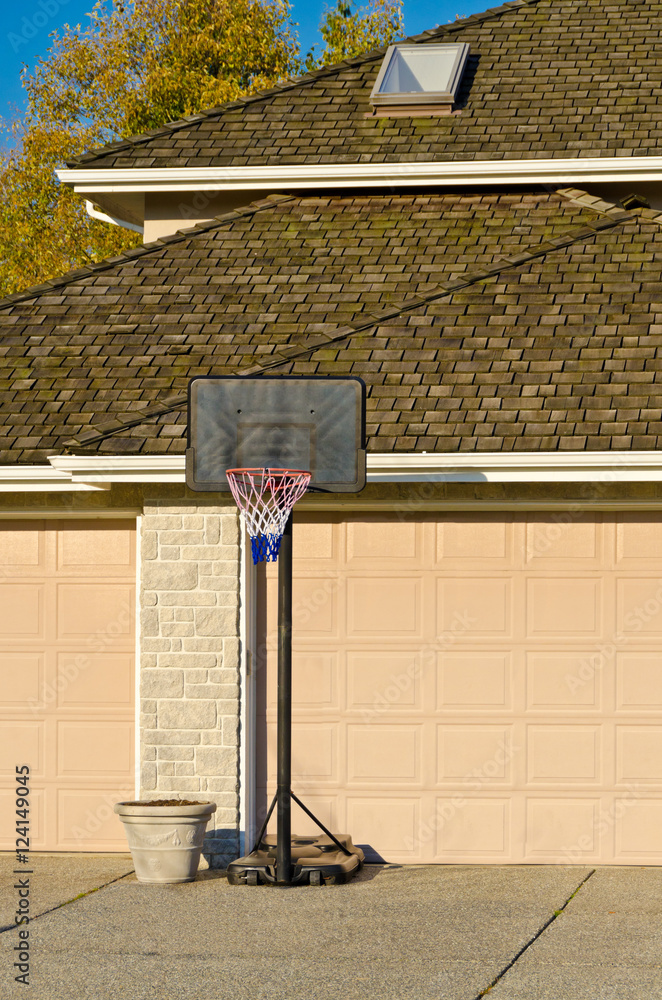 Naklejka premium Basketball Hoop in front of Triple Garage Doors on empty Suburban Residential Home Driveway