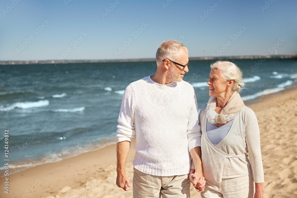 happy senior couple walking along summer beach