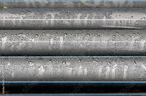 Many industrial black plastic pipes with water drops close-up in perspective.