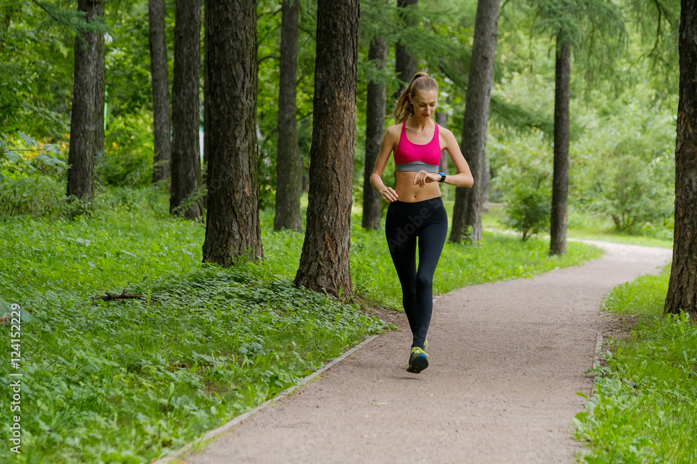 Young slim woman jogging in a park looking to smart watch Young slim woman jogging in a park looking to smart watch