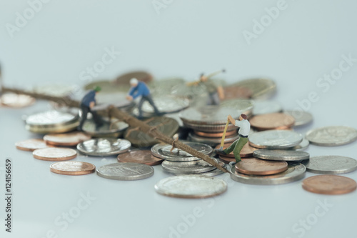 Miniature workmen cutting the tree on pile of coins.