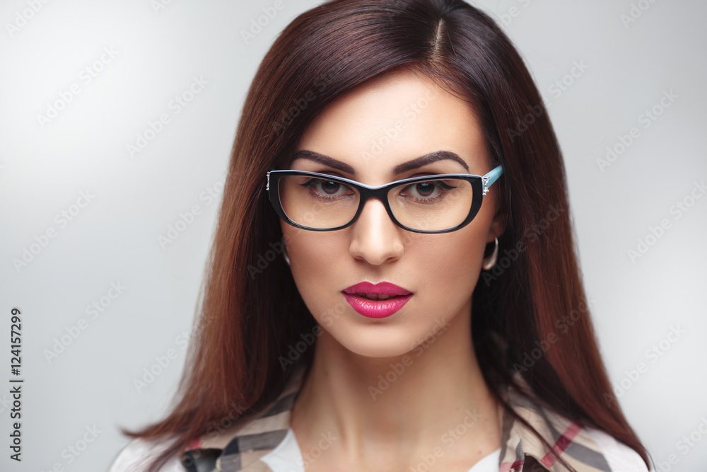Beauty portrait of a beautiful brunette woman wearing glasses isolated on a gray background.