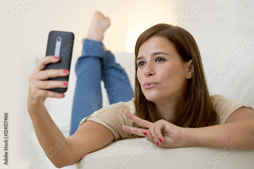 attractive 30 years old woman playing on home sofa couch taking selfie portrait with mobile phone