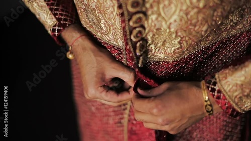 Close-up of man's hands buttoning up Hindu wedding suit