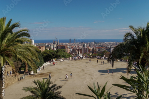 Barcelona, Spain Park Guell Nature Square Placa de la Natura. Visitors on the terrace Hypostyle Room Monumental Zone at Park Guell. Barcelona City visible in the background. Stock Photo Adobe