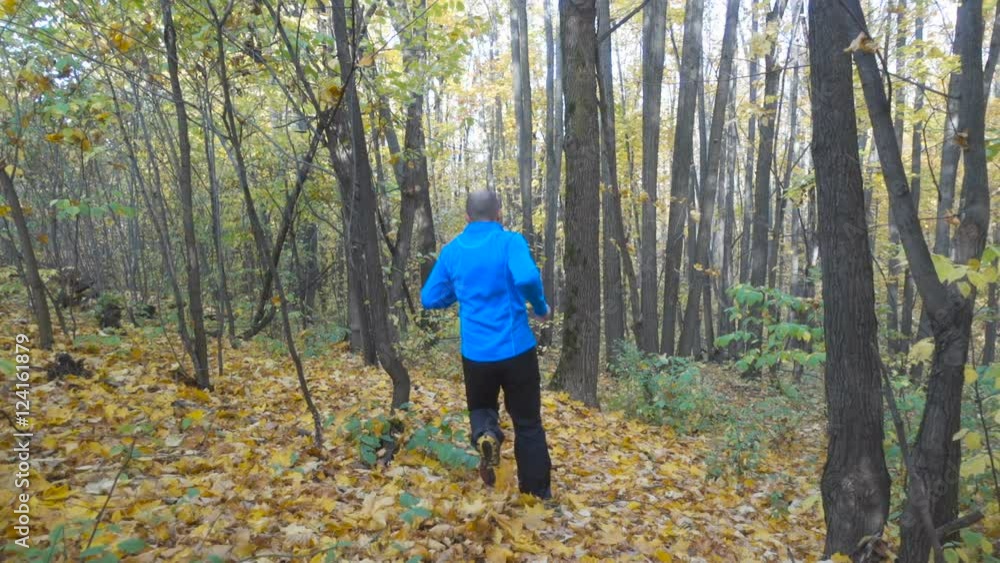 Man jogging cross country running on trail in forest. Training and exercising outdoors when cross country running in inspirational autumn landscape. Sports Motivation. Slow Motion. Man jogging cross country running on trail in forest. Training and exercising outdoors when cross country running in inspirational autumn landscape. Sports Motivation. Slow Motion.