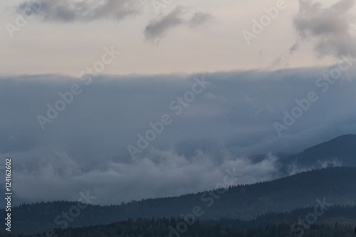 Summer weather phenomenon. Seasonal landscape with morning fog in valley. Clouds drenched valley below the level of the mountain