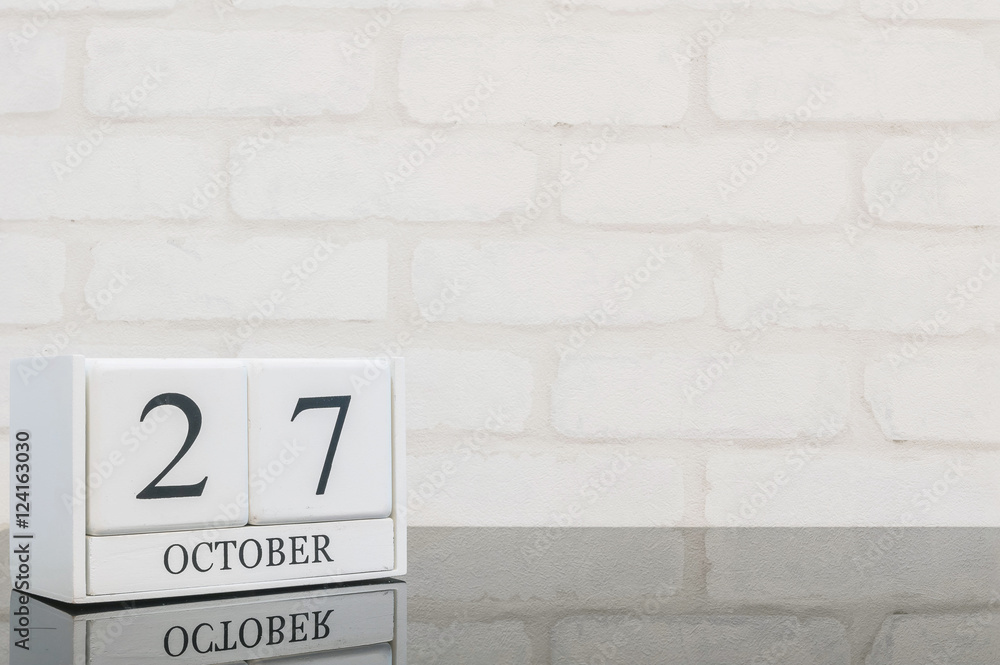 Closeup white wooden calendar with black 27 october word on black glass table and white brick wall textured background with copy space , selective focus at the calendar Closeup white wooden calendar with black 27 october word on black glass table and white brick wall textured background with copy space , selective focus at the calendar
