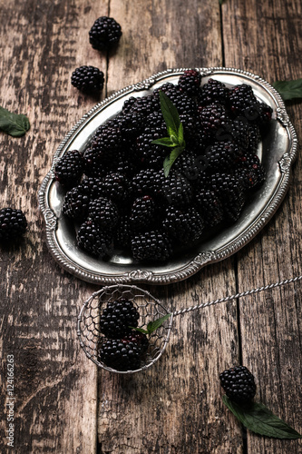 Ripe blackberries in a ceramic bowl on burlap cloth over wooden background close up. Rustic style, Selective focus photo