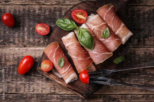 thin slices of prosciutto with mixed with basil, cherry tomatoes on wooden cutting board,vintage background